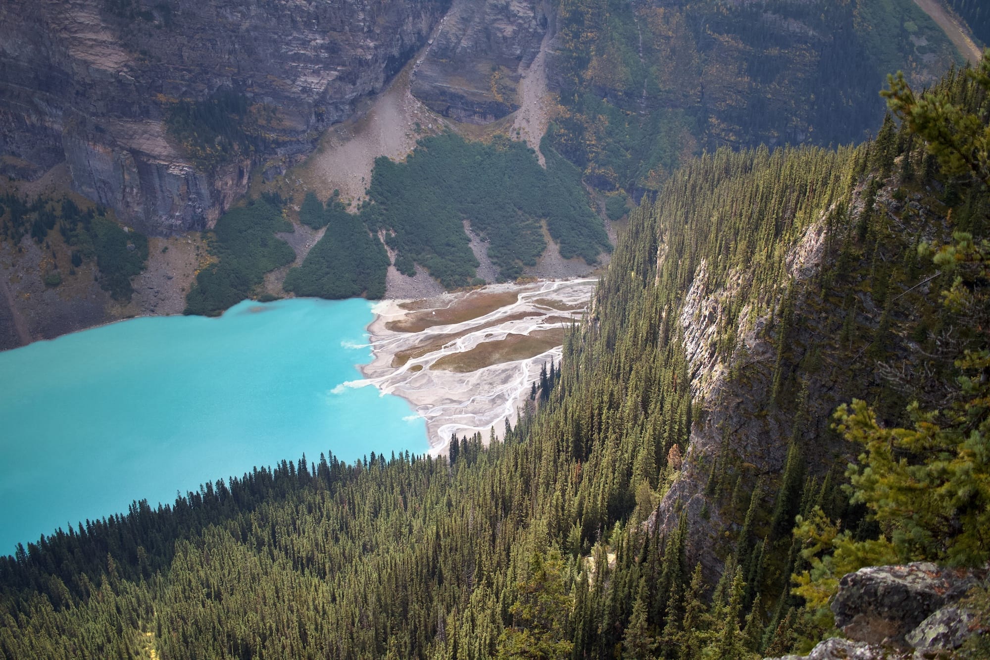 A turquoise lake bordered by a sandy shore and dense evergreen forest, with steep rocky cliffs rising in the background—an ideal setting for environmental consultancy focused on preserving natural landscapes.